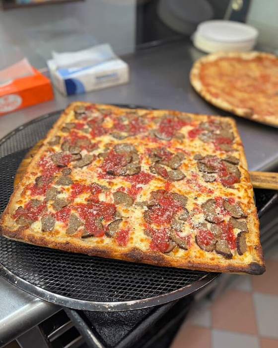 Square Sicilian pizza with meatball and sausage coming off the peel