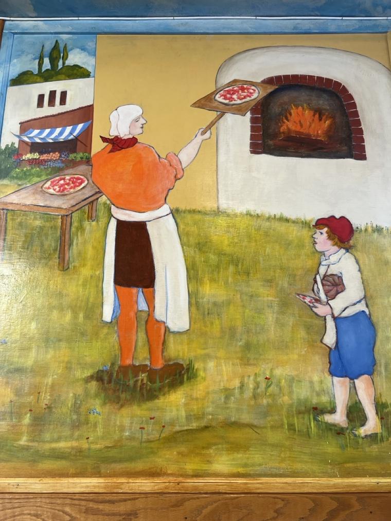 Hand-painted mural of an Italian baker sliding a pizza into a wood-fired oven