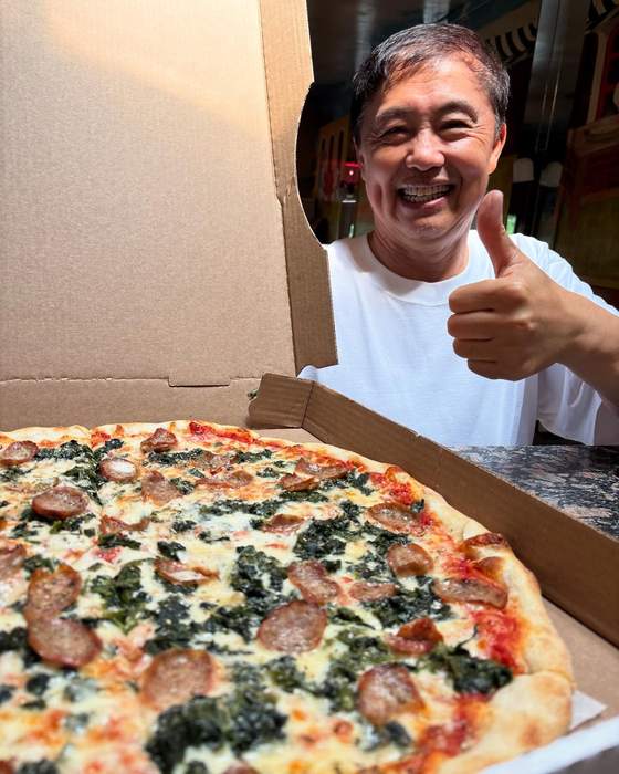 A customer giving a thumbs up over a spinach and sausage white pie
