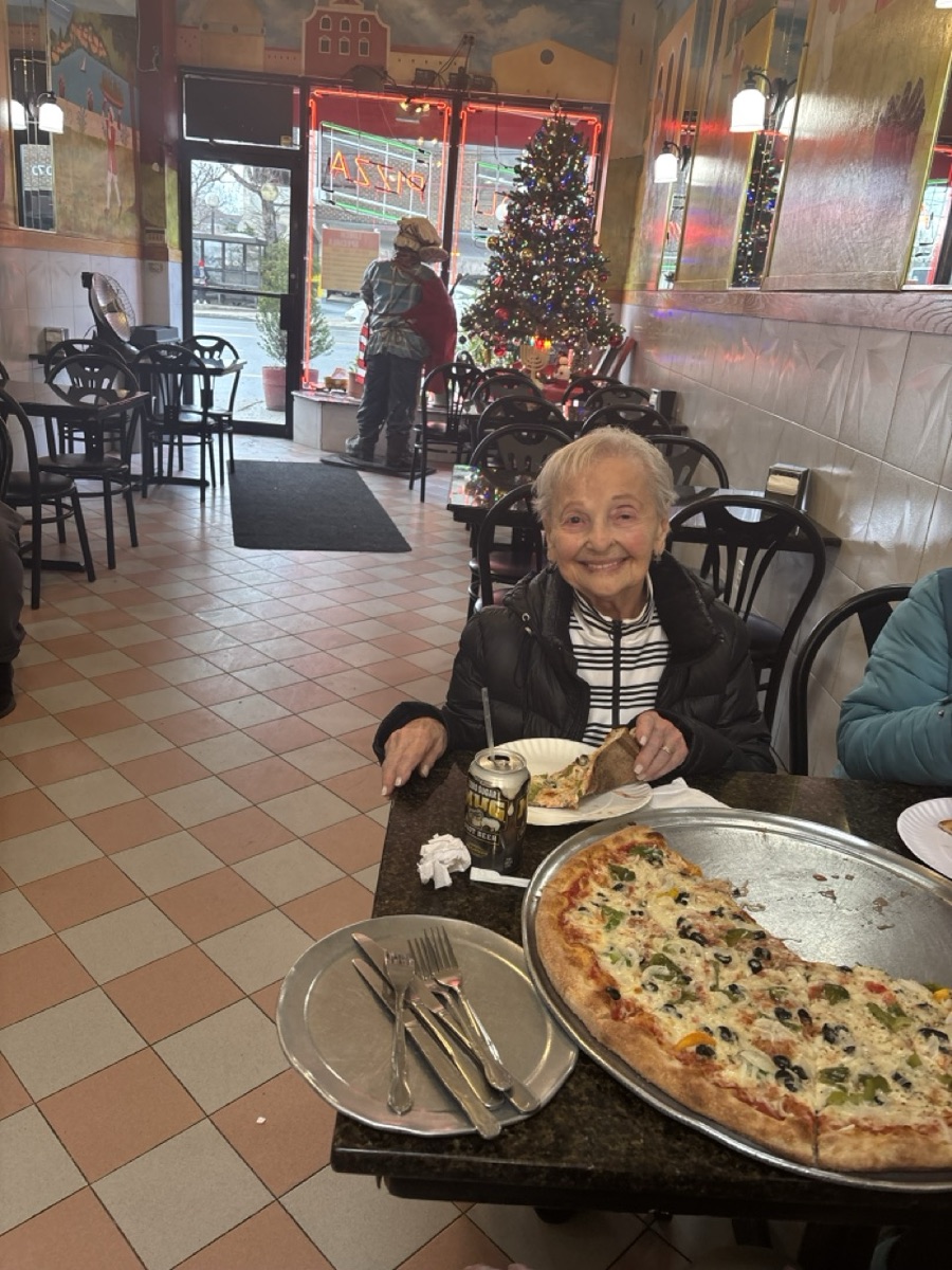 A smiling diner enjoying a slice beside a pizza at Napoli Pizza, with a Christmas tree by the front window